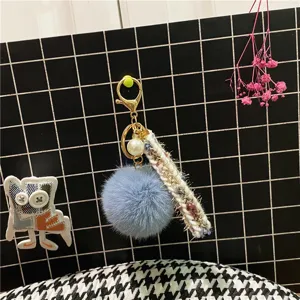 Detailed view of a light blue pom-pom keychain with tweed ribbon and pearl charm