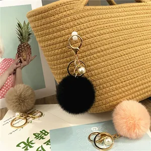 Macro detail of a soft black plush pom-pom keychain with elegant pearl on a straw bag