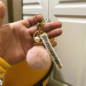 Macro view of pink plush pom-pom keychain featuring an elegant pearl and tweed ribbon charm