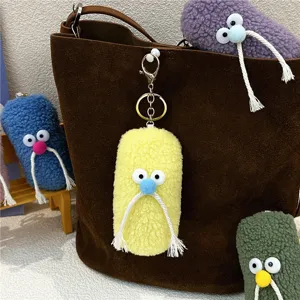 Detail view of quirky plush mustache character keychain charm on a brown leather bag