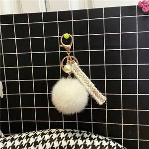 Detail of white faux fur pompom keychain with elegant pearl charm and tweed fabric strap