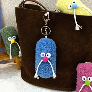 Close-up of quirky blue plush mustache keychain hanging on a stylish brown suede bag