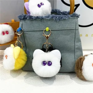 Detail view of plush cat head keychains in multiple colors hanging on a denim bag