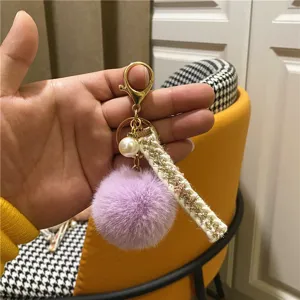 Detail of a purple faux fur pom-pom keychain with pearl charm and gold lobster clasp