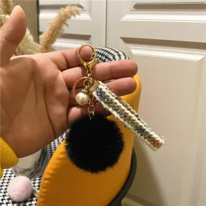 Close-up of a tweed ribbon keychain with black fur pom-pom and pearl decoration