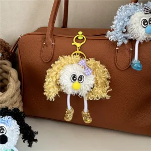 Detail shot of a curly yellow plush monster keychain hanging on a brown leather bag.