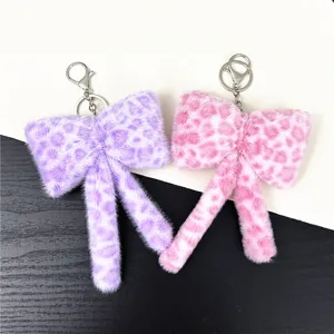 Close-up of purple and pink leopard print plush bow keychains on black and white surface.