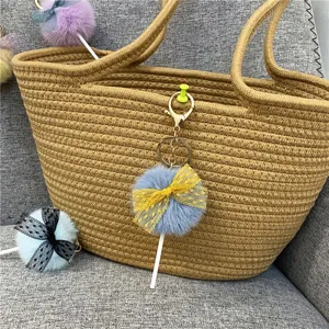 Close-up of a fuzzy pompom lollipop keychain with a lace bow on a woven bag