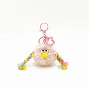 Detail of a pink furry monster keychain with colorful braids and googly eyes