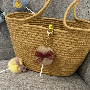 Detail view of a cute plush lollipop keychain with maroon lace bow on a woven bag