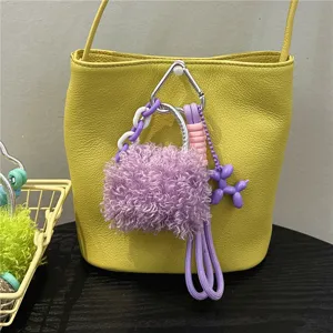 Close-up of purple curly plush bag charm with balloon dog and braided rope on a yellow bag.