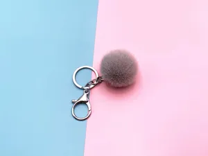 Detailed macro shot of a grey plush pom-pom keychain featuring a sturdy silver lobster clasp.