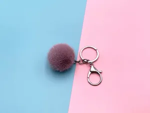 Close-up of fluffy mauve pom pom keychain with silver metal clasp on pink background