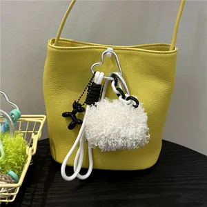 Detail view of a fuzzy white pom-pom and black balloon dog accessory on a yellow bag