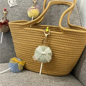 Detailed view of a cute plush lollipop keychain with a lace bow hanging on a woven bag.