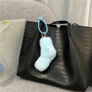 Detail showing a cute light blue plush sock-shaped keychain on a black leather bag