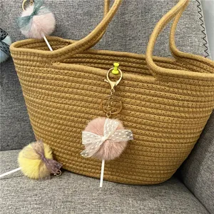 Detail of plush pom-pom lollipop keychain with lace bow on a woven bag