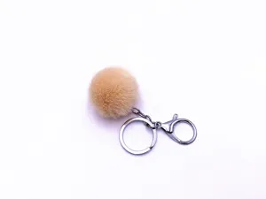 Close-up of fluffy apricot faux fur pom pom keychain with silver metal clasp and ring