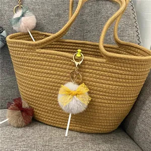 Macro view of cute pom-pom lollipop keychain charms hanging on a woven straw bag.
