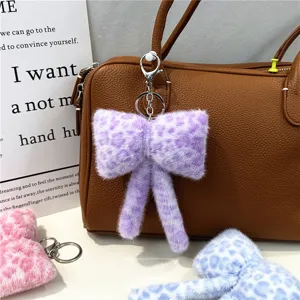 Close-up of a plush purple leopard print bow keychain hanging on a brown handbag
