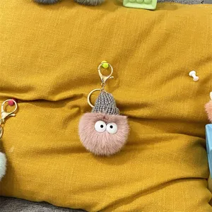 Close-up of a cute fuzzy pink plush keychain with a grey knit hat on yellow fabric.