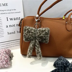 Close-up of a stylish leopard print plush bow keychain hanging on a brown handbag.