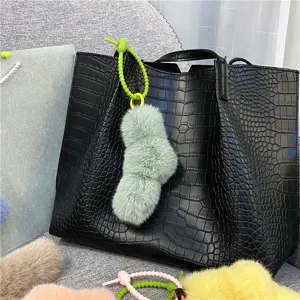 Close-up detail showing a soft mint green plush twist knot charm on a black tote bag.