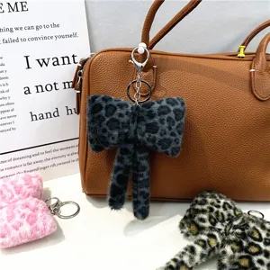 Plush leopard print bow keychain hanging as a stylish charm on a leather handbag