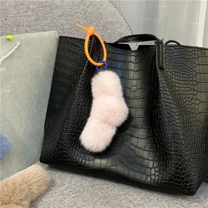 Detail view of a pink plush sock keychain with an orange twist knot on a black bag.