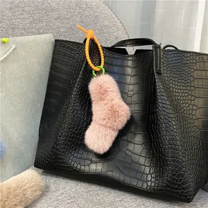 Pink plush sock charm with orange twisted knot hanging on a black crocodile bag