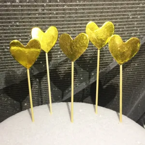Dettaglio di cinque decorazioni per torta a forma di cuore dorato su stecchi in legno.