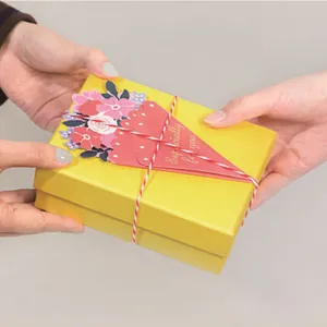 Detailopname van een bloemen wenskaart op een gele geschenkdoos, vastgehouden in de hand