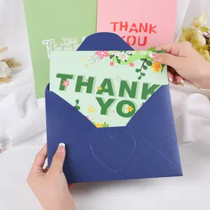 Manos metiendo una tarjeta de agradecimiento 3D floral en un sobre azul marino con corazón.