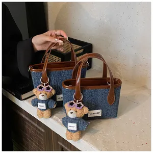 Detail view of denim blue mini bucket bag featuring a cute teddy bear charm accessory