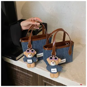 Detailed shot of denim blue bucket bags featuring a cute teddy bear charm and brown handles