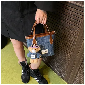Detailed view of the blue denim bucket bag with brown handles and a bear charm.
