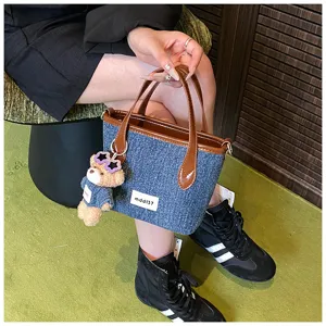 Stylish blue denim bucket bag with brown handles and a cute plush bear charm.