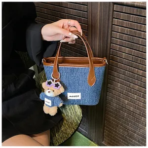 Close-up detail of a denim blue bucket bag featuring brown leather handles and a bear charm