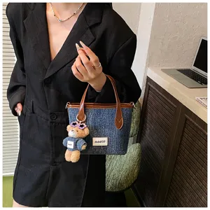 Detail view of a stylish denim blue bucket bag with bear keychain and brown handles.