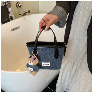 Detailed view of a denim blue bucket bag featuring a cute bear charm held by hand