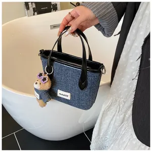 Close-up view of denim blue bucket handbag with cute teddy bear charm and handle