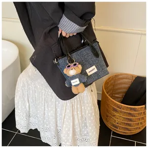 Detailed view of a denim blue minimalist bucket bag with cute bear charm held by model