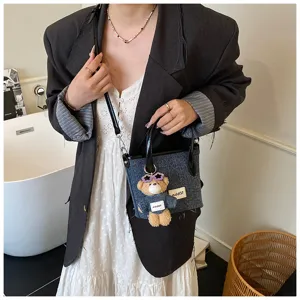 Lifestyle detail of a blue denim bucket bag with a cute bear charm accessory.