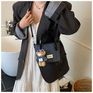 Stylish denim blue bucket bag with cute bear charm worn as a crossbody handbag.