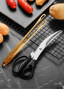 Detailansicht von Küchenschere aus Edelstahl und goldener Grillzange auf einem Gitter.