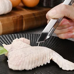 Stainless steel kitchen tweezers plucking feathers from raw chicken wing on black plate.