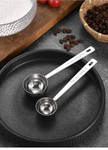 Dettaglio di misurini per caffè in acciaio inox da 15 ml e 30 ml su un piatto nero