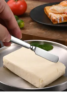 Close-up of stainless steel butter spreader knife slicing through a fresh butter block