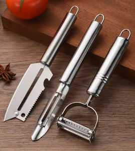 Close-up detail of three different stainless steel kitchen peelers on a wooden board.