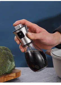 Close-up view of a hand holding a stainless steel glass oil sprayer in a modern kitchen.